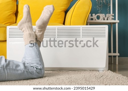 Young woman in warm winter socks near electric heater. Concept of heating season
