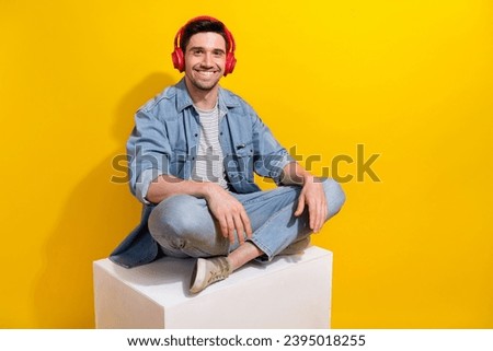 Photo of positive funky guy wear denim jacket sitting white platform listening music empty space isolated yellow color background Royalty-Free Stock Photo #2395018255