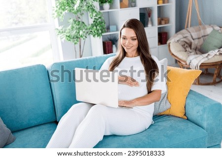 Photo of charming lovely girl future mama mommy sitting on couch watching movie listening podcast comfortable room indoors