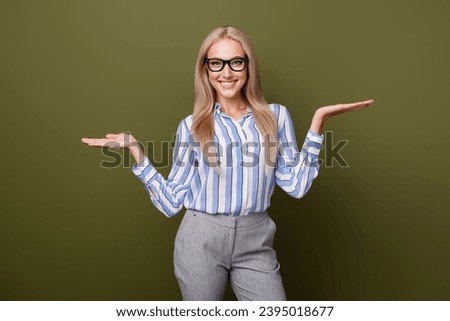 Photo portrait of blonde lovely young lady palms compare empty space dressed stylish striped garment isolated on khaki color background