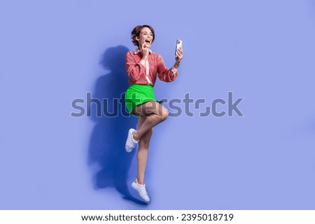 Full size photo of adorable positive woman dressed print shirt flying look at smartphone read post isolated on blue color background