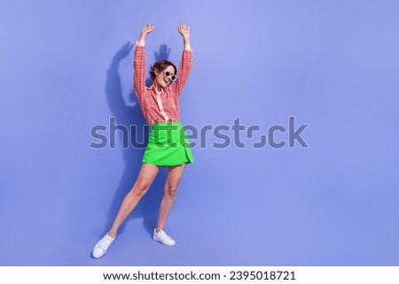 Full size photo of satisfied optimistic woman dressed print shirt in sunglass holding hands up have fun isolated on blue color background