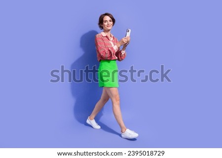 Full size photo of good mood lovely woman dressed print shirt holding smartphone walk to empty space isolated on blue color background