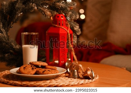 Christmas cookies with glass of milk and decor on table in room at night, closeup