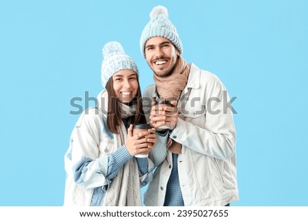Loving couple in winter clothes with coffee cups on blue background