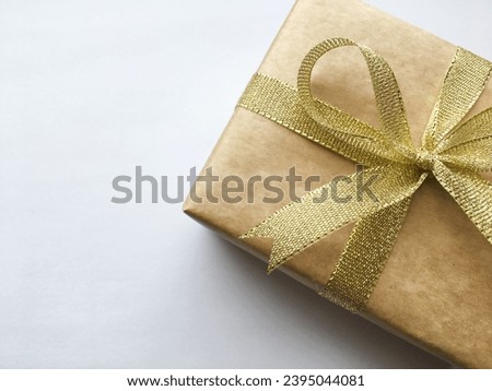 Gift box with a golden satin ribbon bow close-up on a light background
