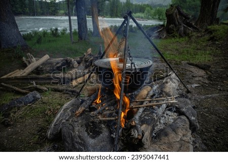 Tourists prepare lunch in a camping pot on a campfire. Cooking in the forest on the banks of a mountain river outdoors. Travel camp, campfire site. 