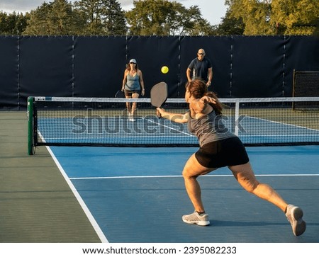 A female pickleball player returns a backhand shot in a mixed doubles match. Royalty-Free Stock Photo #2395082233