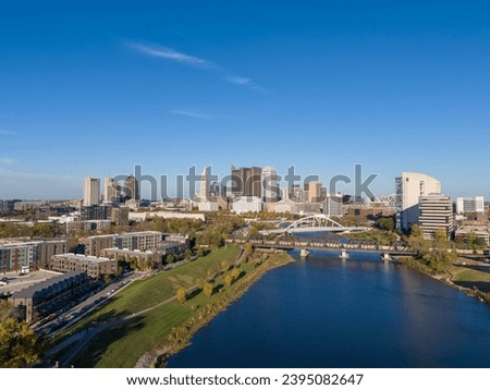 Columbus, OH skyline by the Scioto River, with clear skies and lush greenery around.