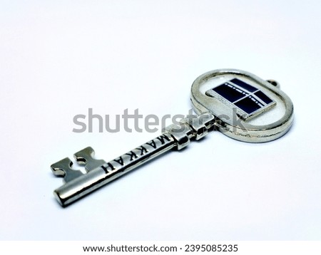 The key chain has an ornamental pattern and a picture of the Kaaba. Isolated on white background.