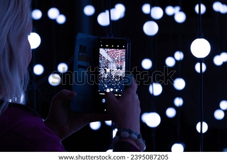 
Woman takes a photo with her smartphone in an interior with white lights an light balls 
