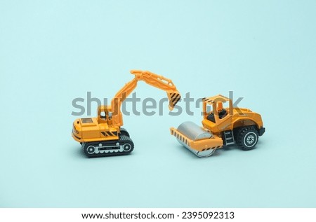 Toy asphalt paver and excavator on blue background