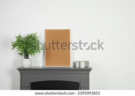 Empty frame, candles and potted houseplant on fireplace near white wall indoors, space for text. Interior design