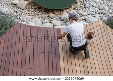 Hardwood deck oil application, overhead woman painting wood boards of garden decking Royalty-Free Stock Photo #2395096069