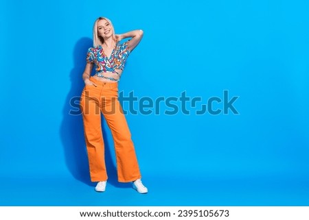 Portrait of gorgeous adorable girl wear stylish shirt orange pants hand in pocket arm on neck isolated on vivid blue color background