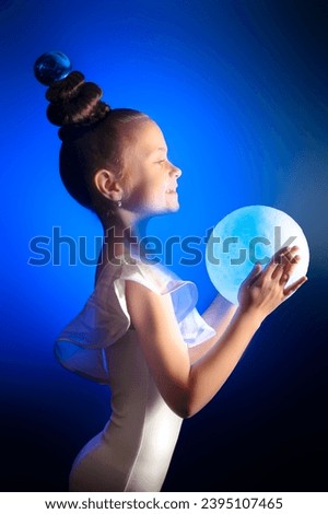 Girl gymnast in white gymnastic leotard with glowing blue ball in hands on blue background