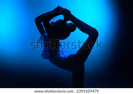 Silhouette of a girl gymnast doing an acrobatic stretching exercise. Blue background