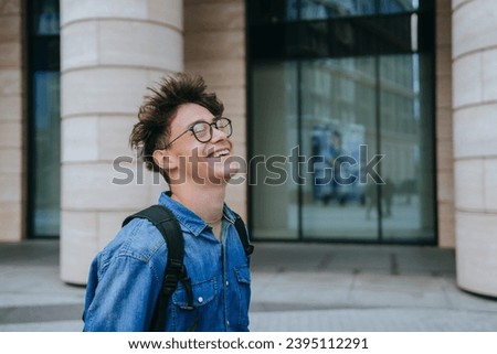 Laughing teenager walking at street carrying backpack goes to college.Handsome schoolboy in glasses smiles wide eyes closed. Education, college life.