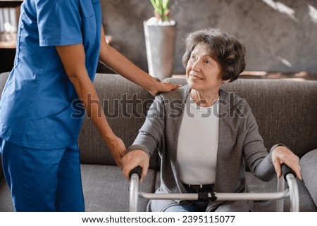 Cropped photo of happy pensioner grandmother elderly patient with walking frame with assistance of nurse caregiver at home. Walking after trauma injury Royalty-Free Stock Photo #2395115077