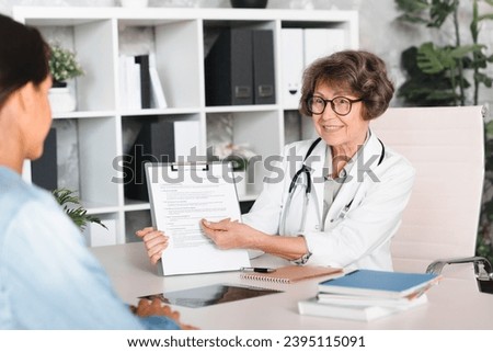 Medical worker doctor therapist family doctor showing explaining medical insurance, papers, diagnosis, test results to female patient at hospital. Signing papers
