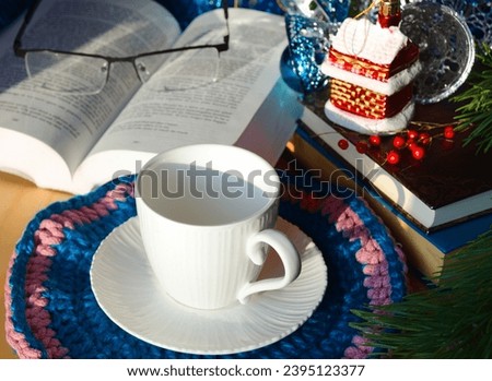 An empty cup for tea or coffee against a background of books and green Christmas tree branches. Decorations for the New Year and Christmas. A place for congratulations.
