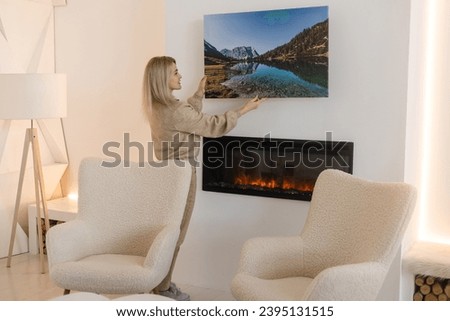 Young woman hanging a photo canvas painting on the wall