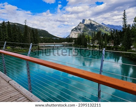 Guide rails of a pedestrian bridge crossing an emerald perfectly reflecting river Royalty-Free Stock Photo #2395132211