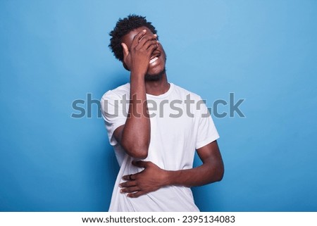Uplifting and joyous after hearing amusing joke, African American man with afro hair bursts into laughter while placing his hands on his eyes and stomach. Positive feelings and humor.