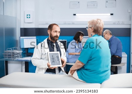 During medical checkup, healthcare specialist shows picture of human skeleton on tablet to elderly patient. Male doctor holds up gadget that displays examination of bones and diagnoses osteopathy.