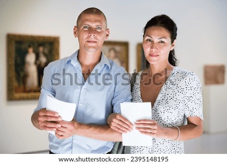 Wife and husband standing in picture gallery and watching paintings
