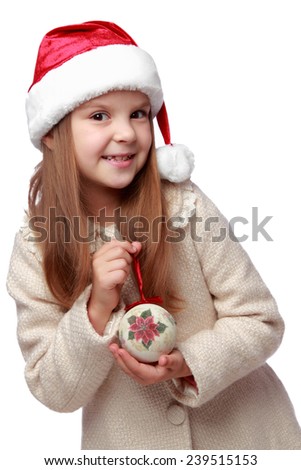 laughing little girl in Santa hat holding Christmas decoration in hands/Studio image of a charming joyful little girl with long blond hair in Santa hat holding christmas ball isolated on white