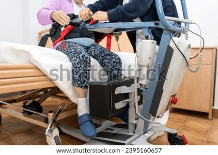 A care staff using a power assist to lifts a patient at nursing home. High quality photo Royalty-Free Stock Photo #2395160657