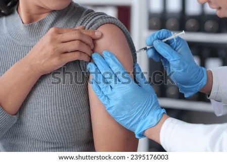 Asian woman receives flu vaccine at hospital Hands of a male doctor or professional nurse in medical gloves injecting antiviral medicine to a patient. treatment concept medical services. Royalty-Free Stock Photo #2395176003