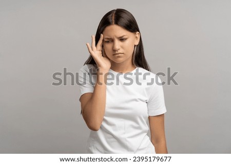 Tired exhausted teen girl feeling headache holding temple by hand on grey background. Upset teenager suffers head pain, migraine, cephalalgia, hypertension, premenstrual syndrome concept. Royalty-Free Stock Photo #2395179677