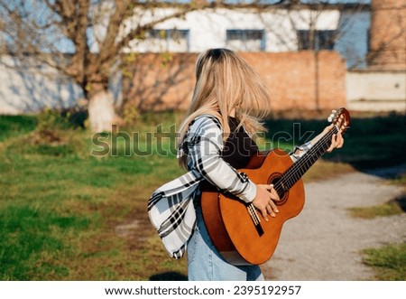 The girl plays the guitar. The girl is spinning on the street, on a bright sunny day.Learning music. Composer and author. Generation z.