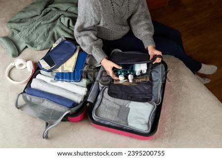The girl puts cosmetics in a suitcase with clothes and accessories for the trip. Travel concept.