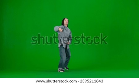 In the frame on a green background, a limp. Dances young, beautiful girl. Demonstrates dance moves in the style of hip hop. Shes staring at the camera. Shes dressed in loose clothes, street style