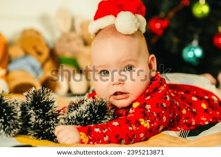 Newborn baby boy in a red Santa hat lies on the bed near the Christmas tree