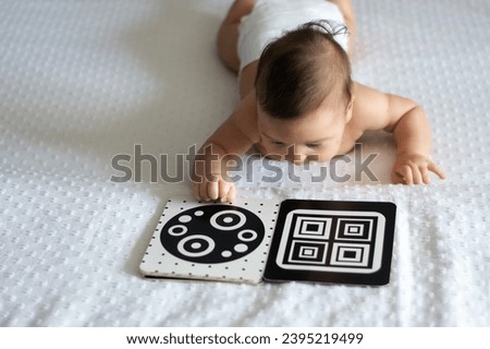 A baby looks at a black and white contrast educational book. Intellectual development of newborns. Developing cards for children. Royalty-Free Stock Photo #2395219499