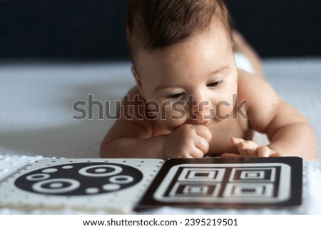A baby looks at a black and white contrast educational book. Intellectual development of newborns. Developing cards for children. Royalty-Free Stock Photo #2395219501