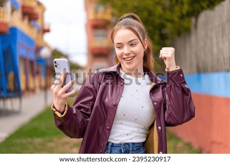 Young pretty girl using mobile phone at outdoors celebrating a victory