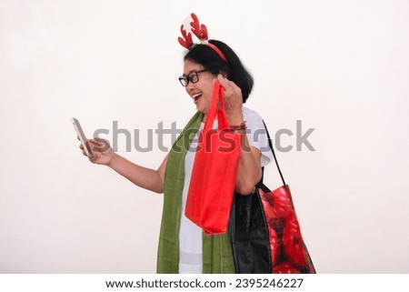 Woman standing alone showing red Christmas shopping bag in her video call using smartphone in her hand