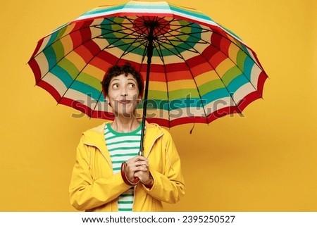 Young happy woman wear waterproof raincoat outerwear red hat hold in hand umbrella look overhead isolated on plain yellow background studio portrait. Outdoors lifestyle wet fall weather season concept