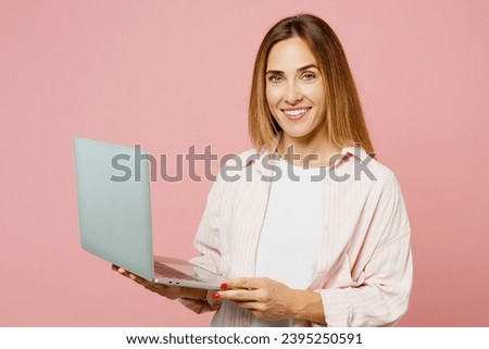 Young smiling happy cheerful IT woman she wear shirt white t-shirt casual clothes hold use work on laptop pc computer isolated on plain pastel light pink background studio portrait. Lifestyle concept