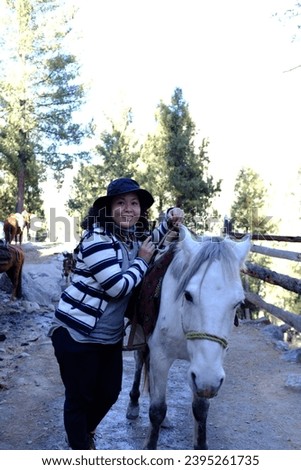A asian female tourist posing for a picture with a white horse, on the path towards Fairy Meadows in Pakistan.