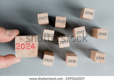 Photo of wooden block group with gray numbers of passed years and one of them hold by a human hand with red number 2024 imprinted on wooden surface. New Year, Strategy and Standing Out concept.