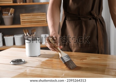 Man varnishing wooden surface with brush indoors, closeup Royalty-Free Stock Photo #2395264313