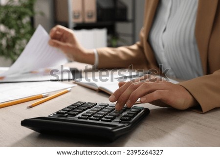 Woman using calculator while working with document at wooden table, closeup