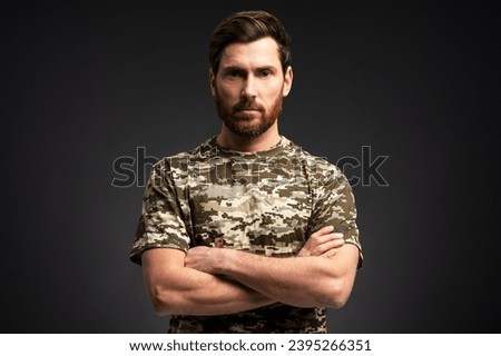 Portrait serious soldier holding arms crossed wearing military camouflage uniform looking at camera isolated on black background, copy space
