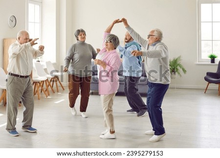 Retirement community. Elderly men and women actively spend time having fun and dancing at party in nursing home. Group of senior Caucasian people laughing and dancing together in living room. Royalty-Free Stock Photo #2395279153